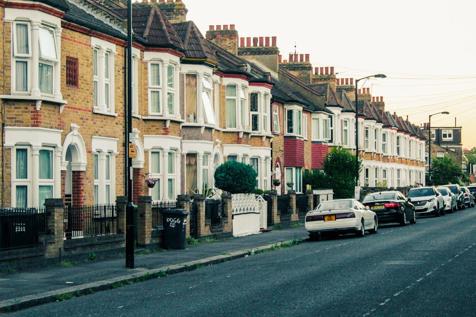 A row of terraced houses on Angell Town estate with brick and white painted facades, bay windows, and small front gardens enclosed by low brick walls and black iron railings. Several houses have open